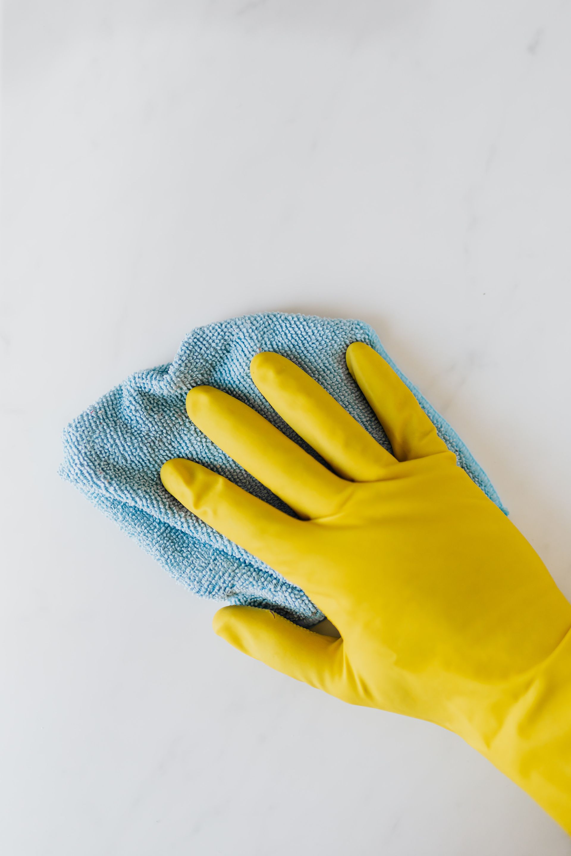 Hand in yellow glove wiping a white surface with a blue cleaning cloth.