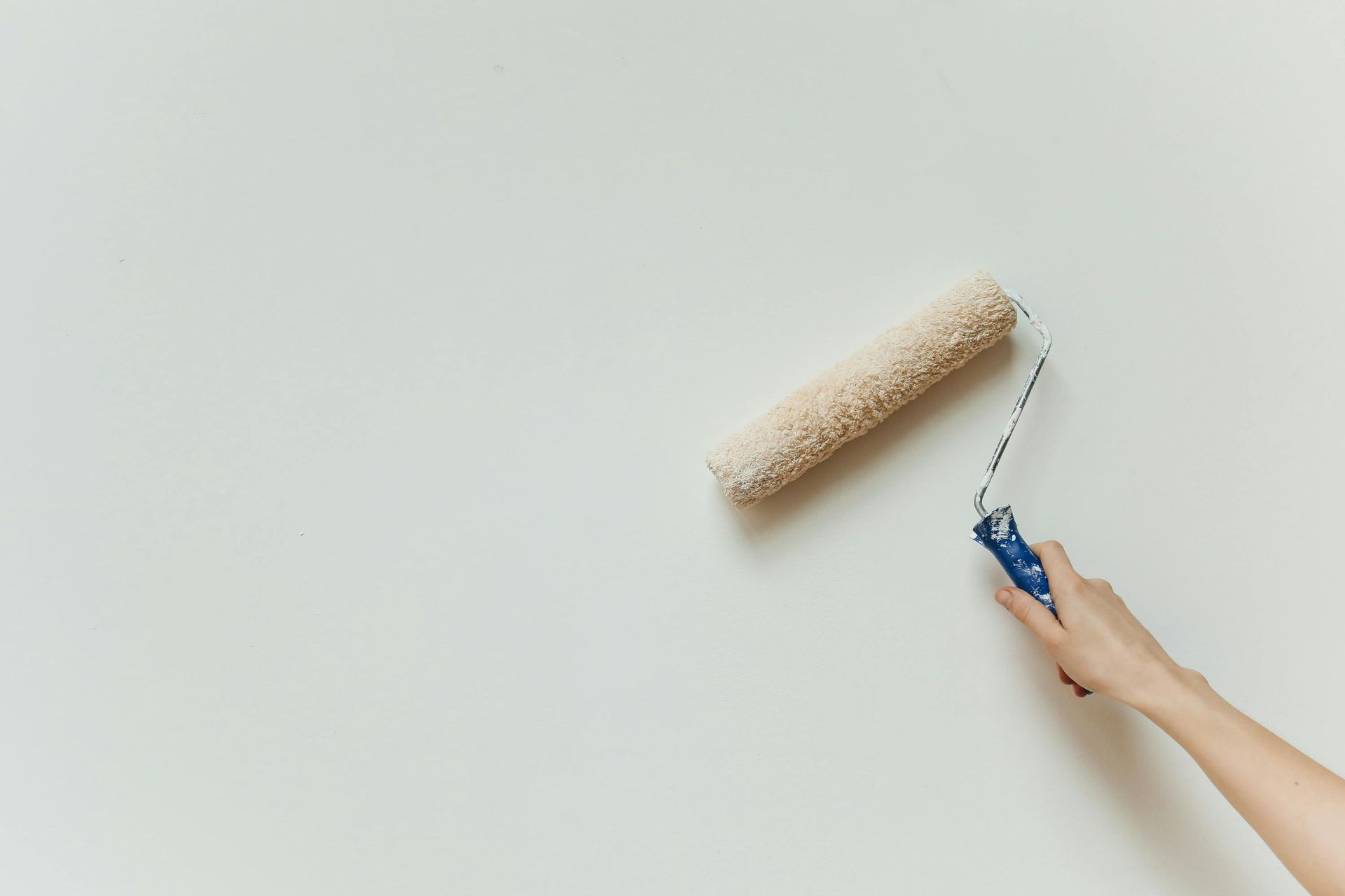 A person's hand holding a paint roller against a blank, light-colored wall.