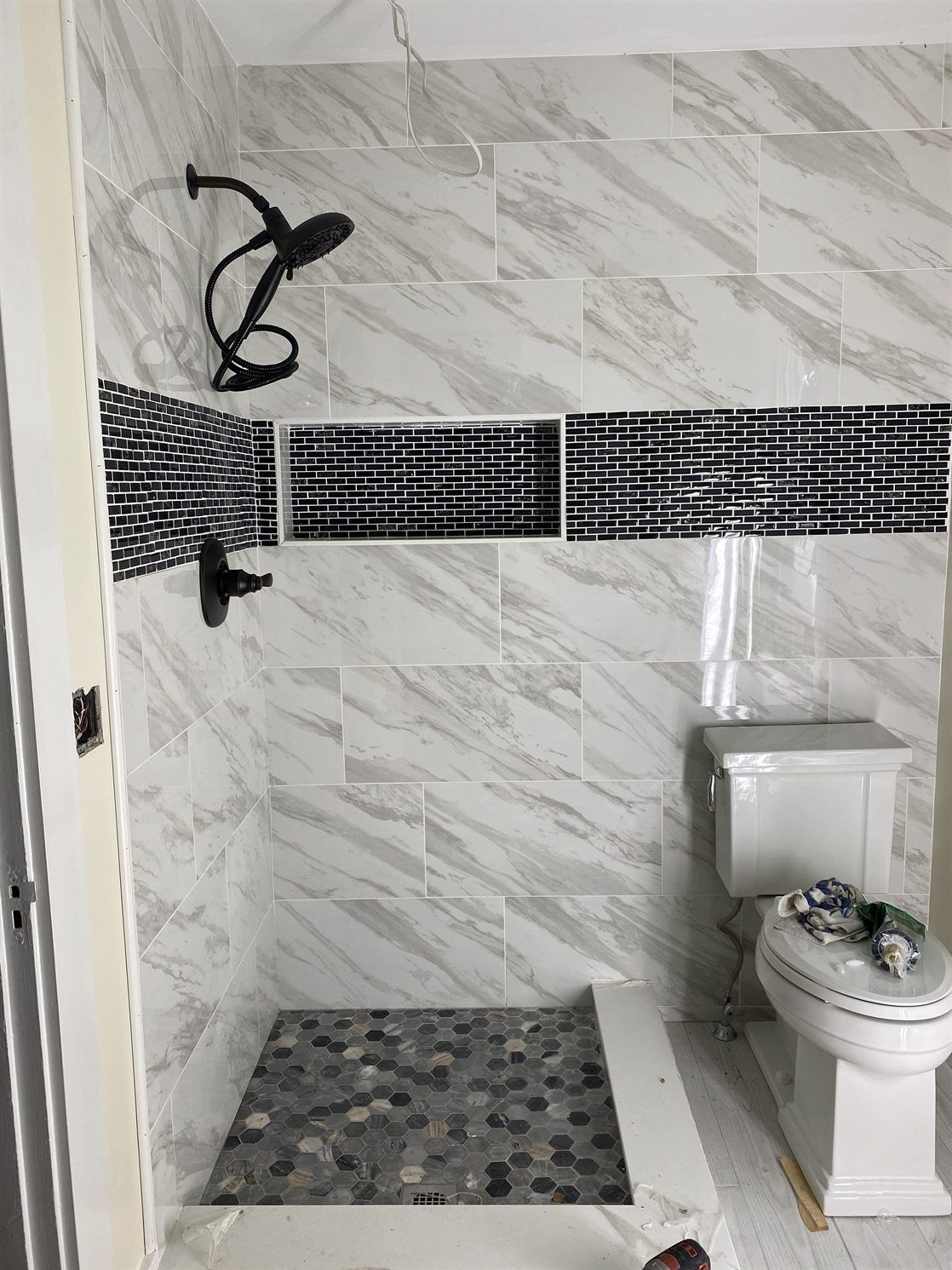 A bathroom with a toilet , shower and shower head.