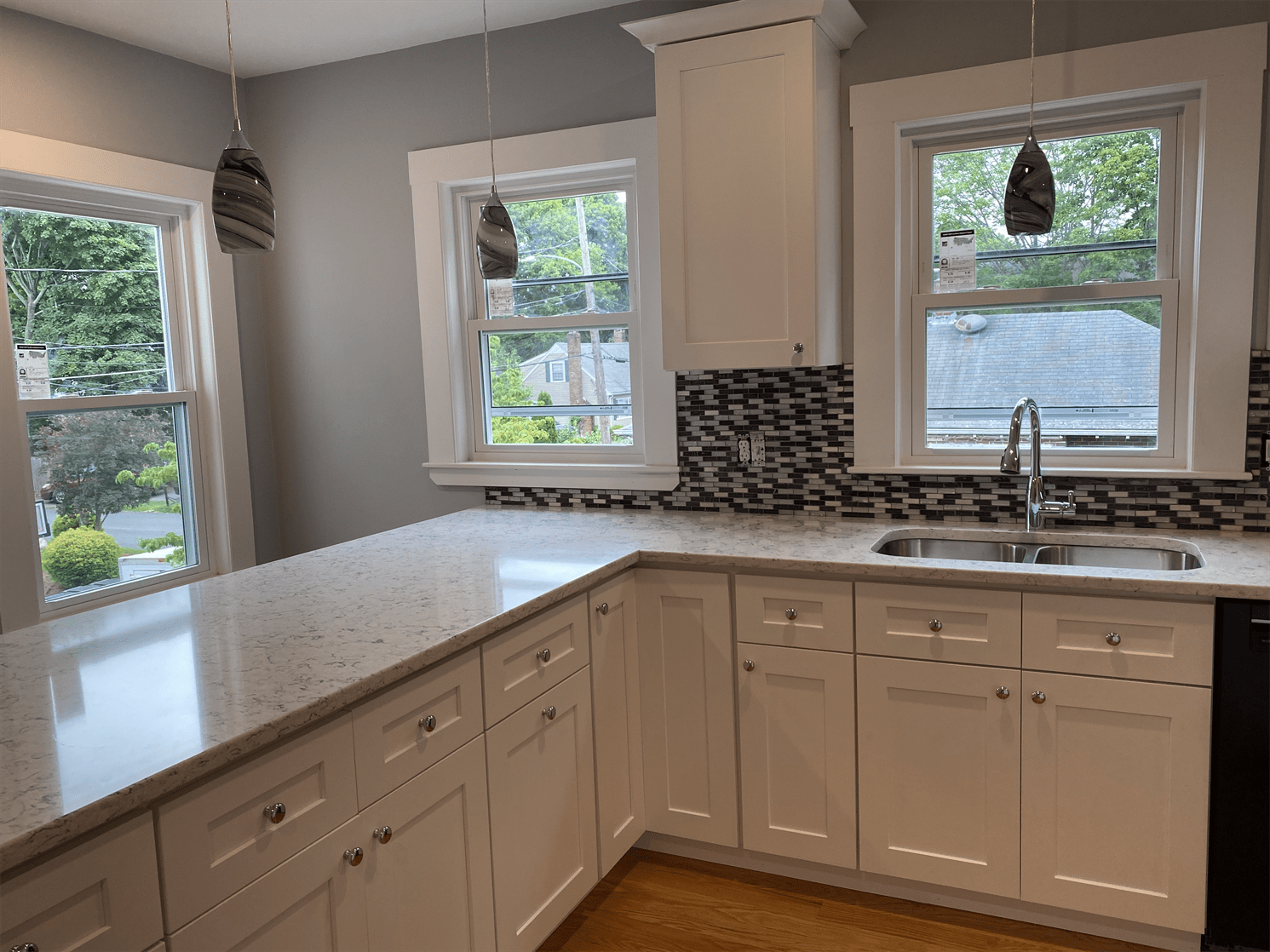 A kitchen with white cabinets , a sink , and two windows.