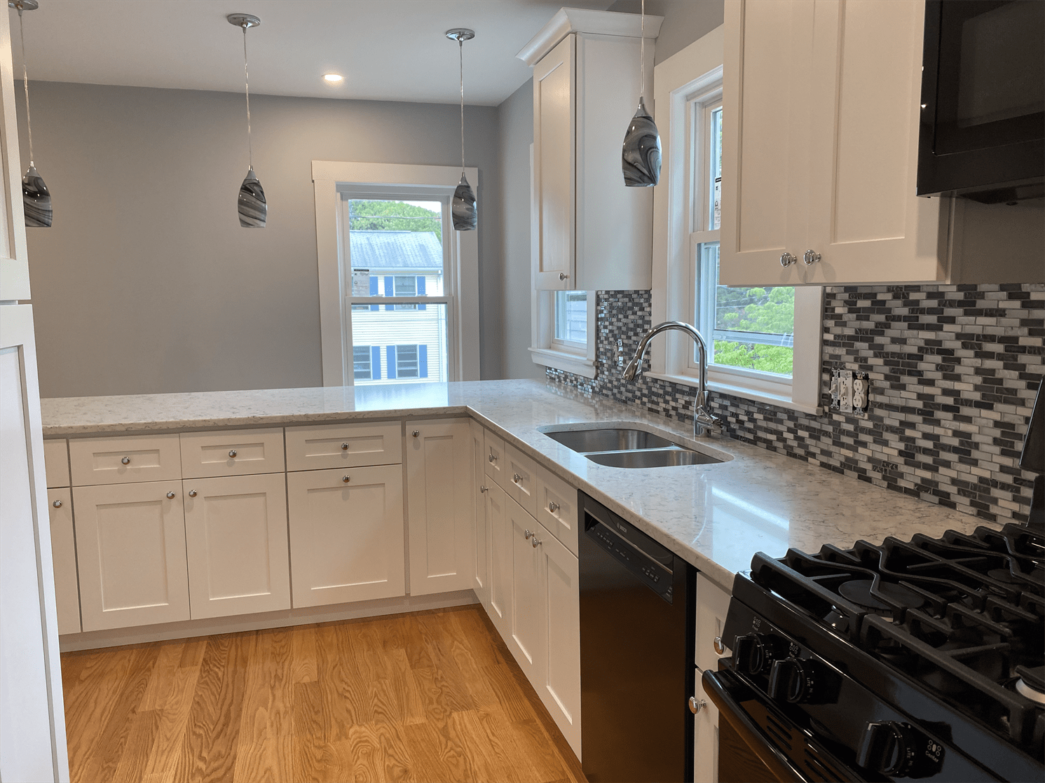 A kitchen with white cabinets , a stove , a sink , and a window.