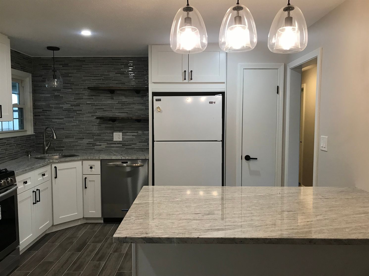 A kitchen with white cabinets , a refrigerator , a dishwasher , and a large island.