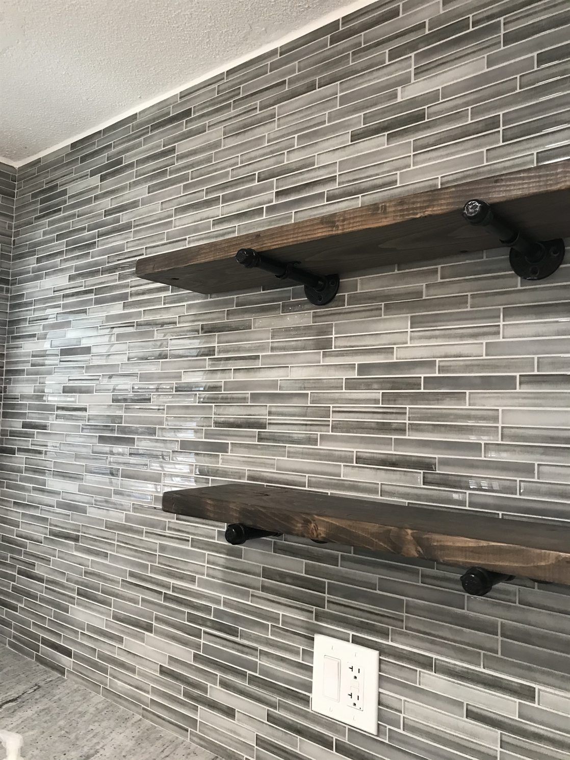 Three wooden shelves are sitting on a tiled wall.