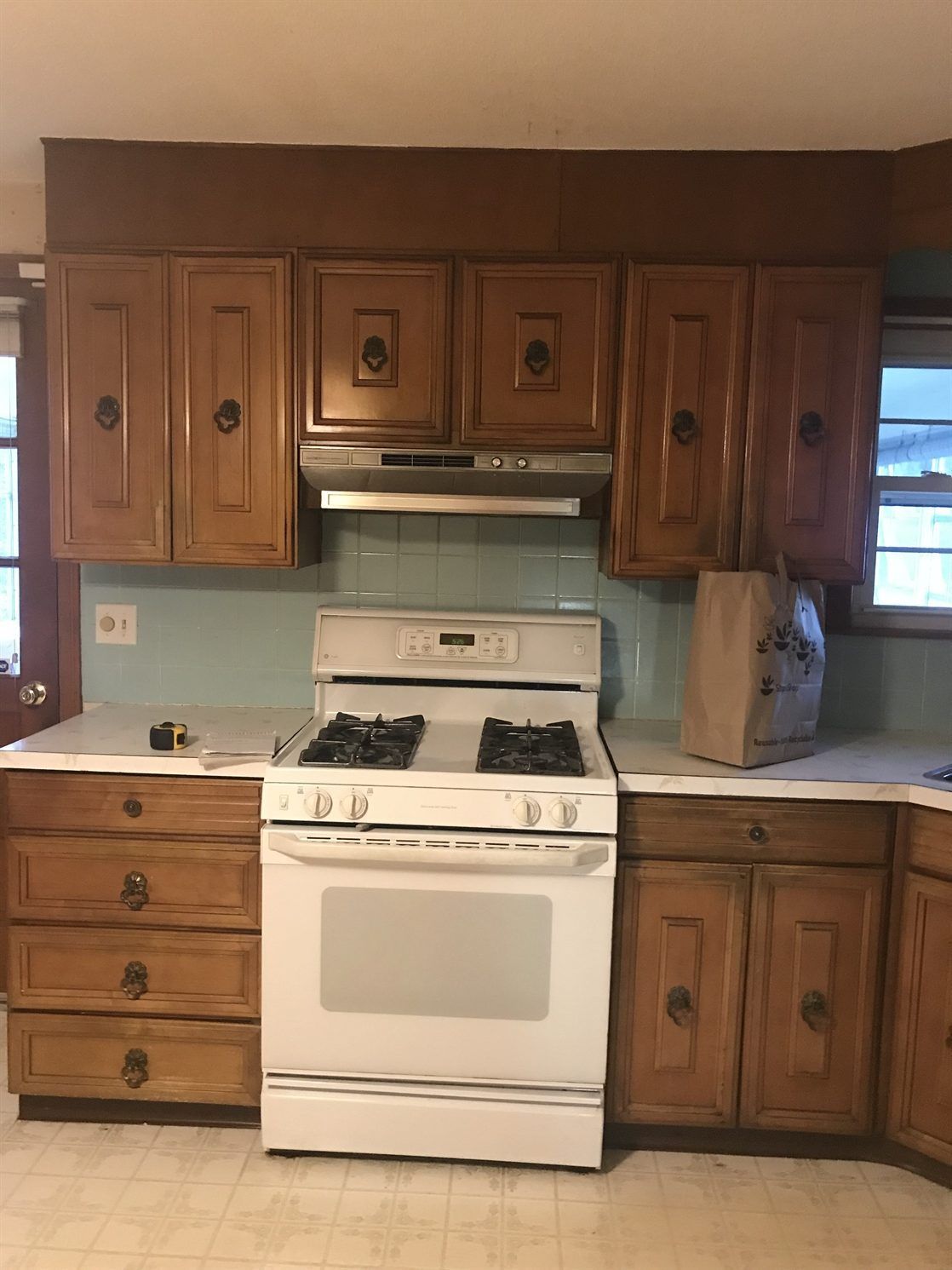 A kitchen with wooden cabinets , a stove , and a window.