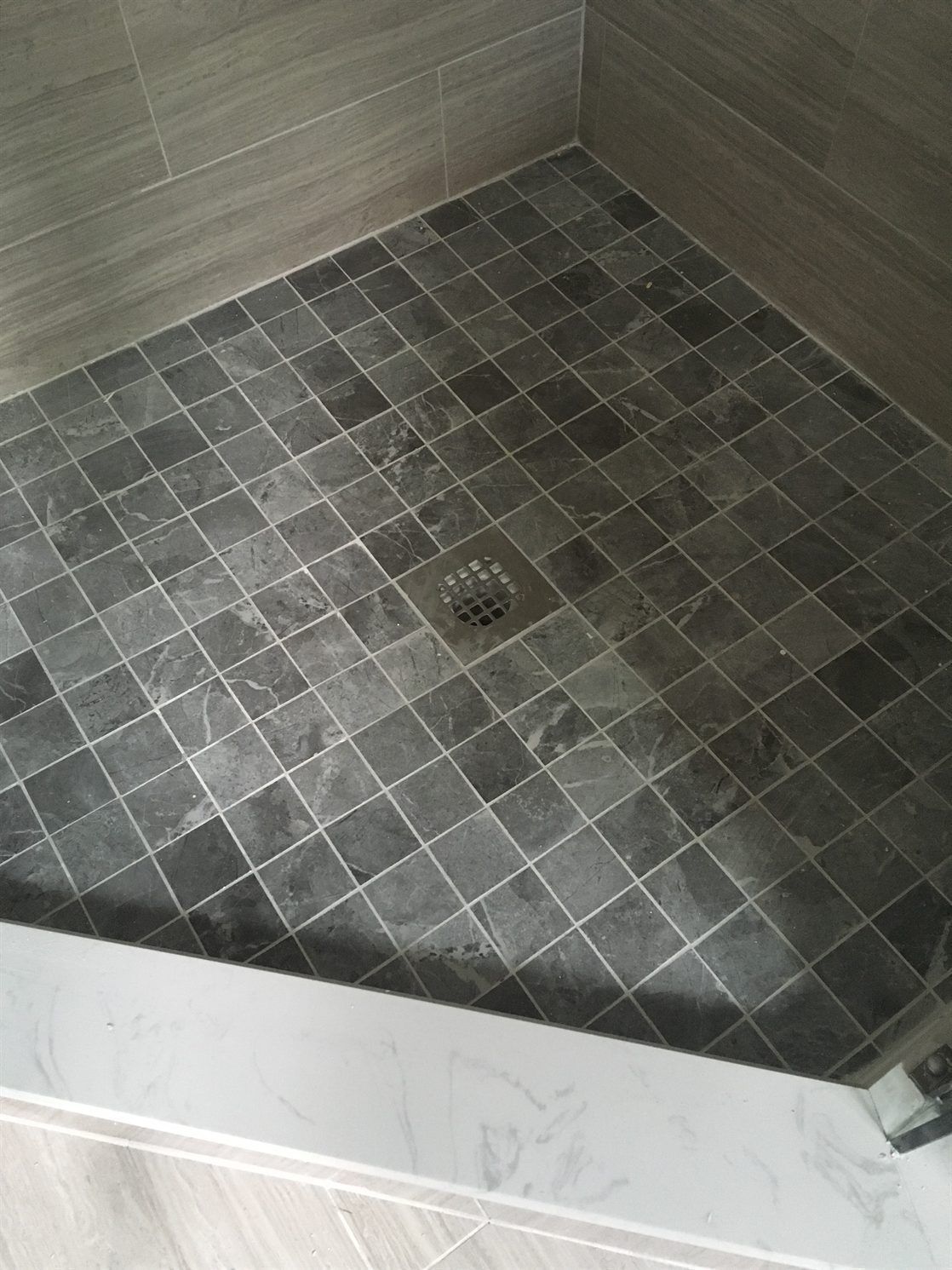 A shower stall with a black tile floor and a drain.