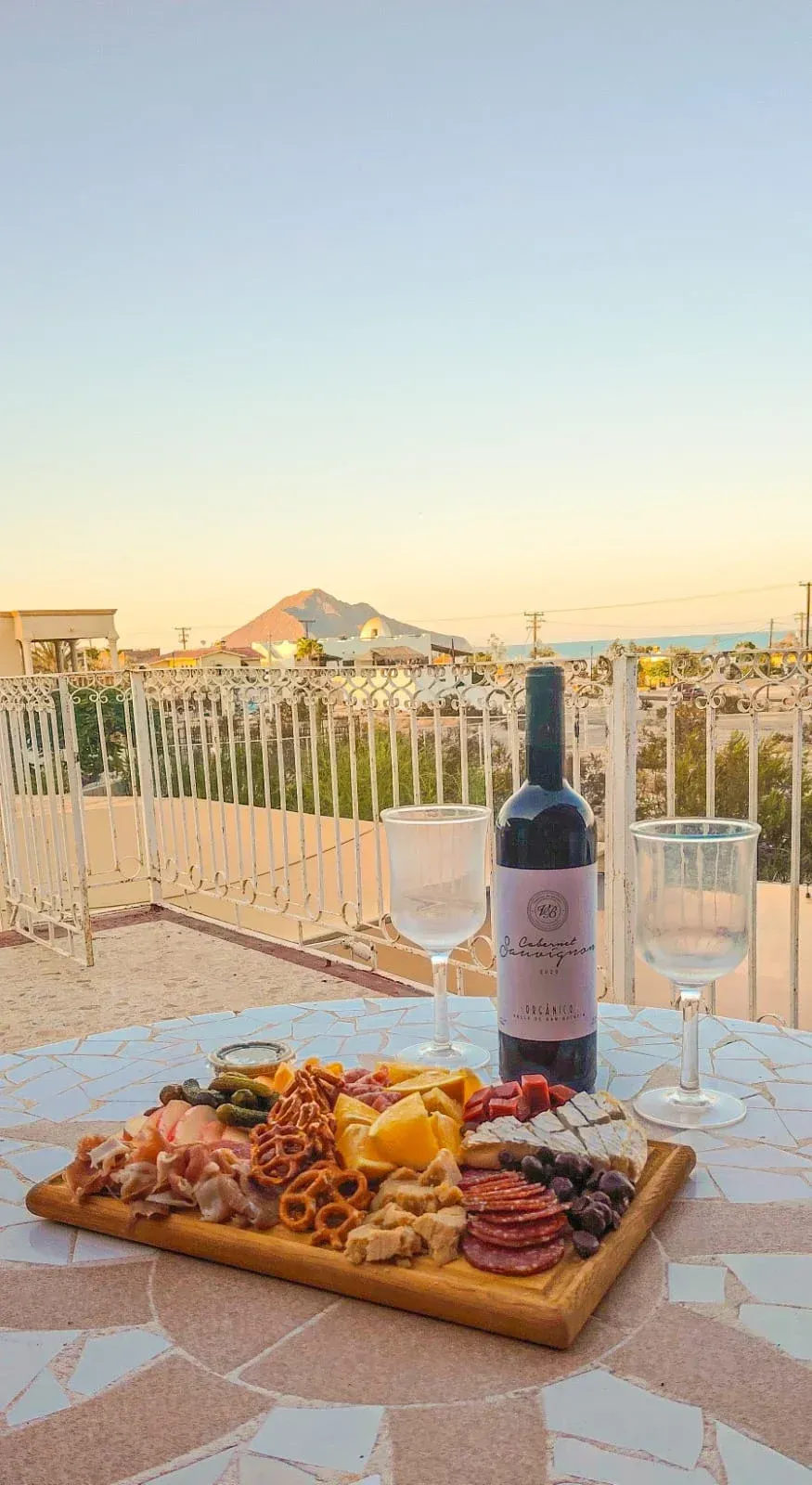 Tabla de embutidos con vino y copas en una azotea con vistas a una ciudad al atardecer.
