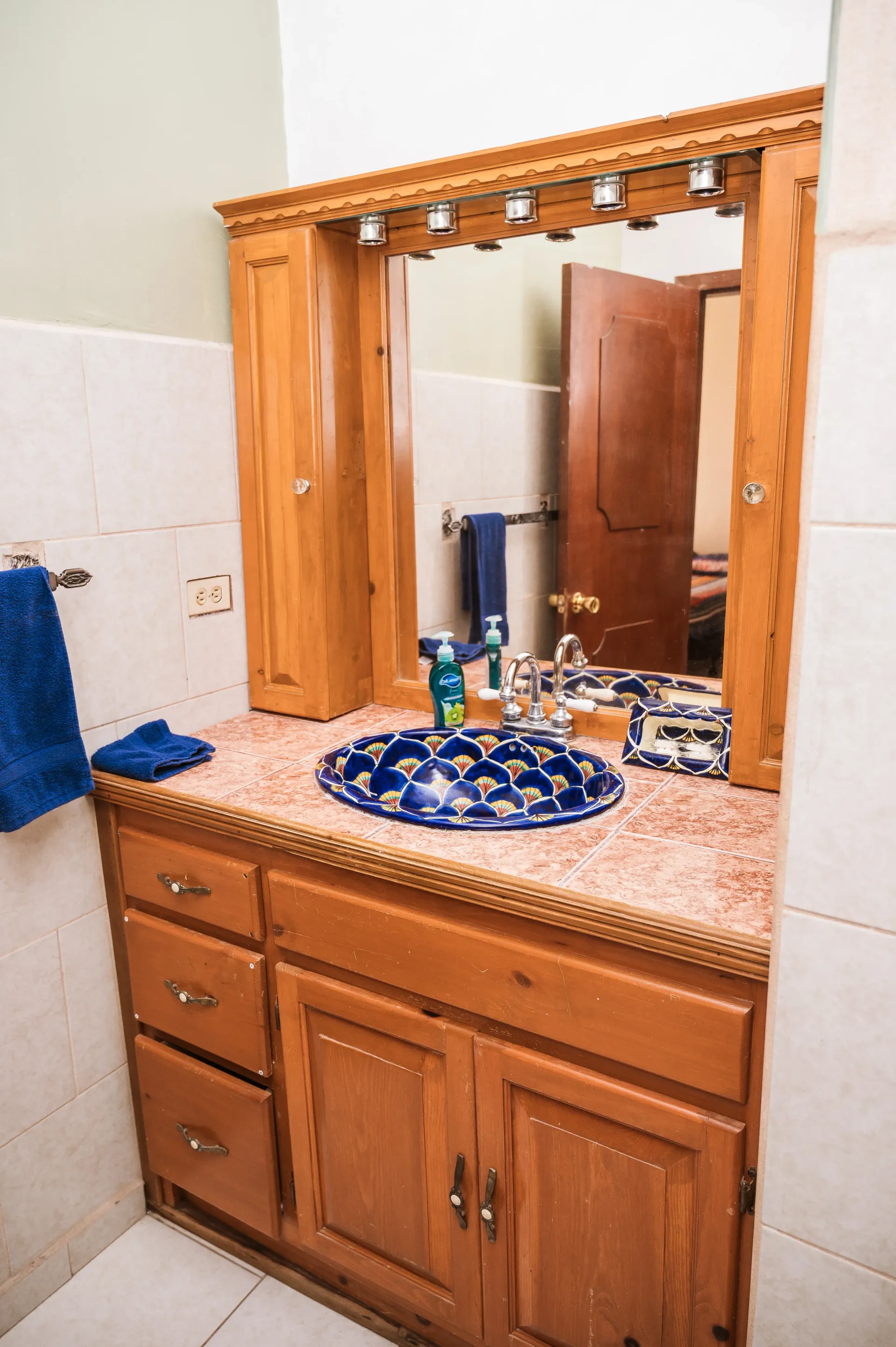 Mueble de baño con gabinetes de madera, lavabo floral azul y espejo.