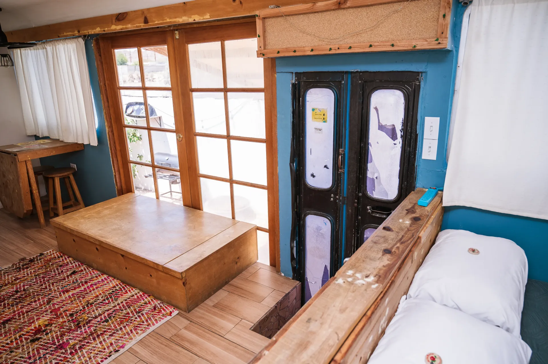 Cozy interior with wooden accents, blue walls, a bed, and a window overlooking the outdoors.