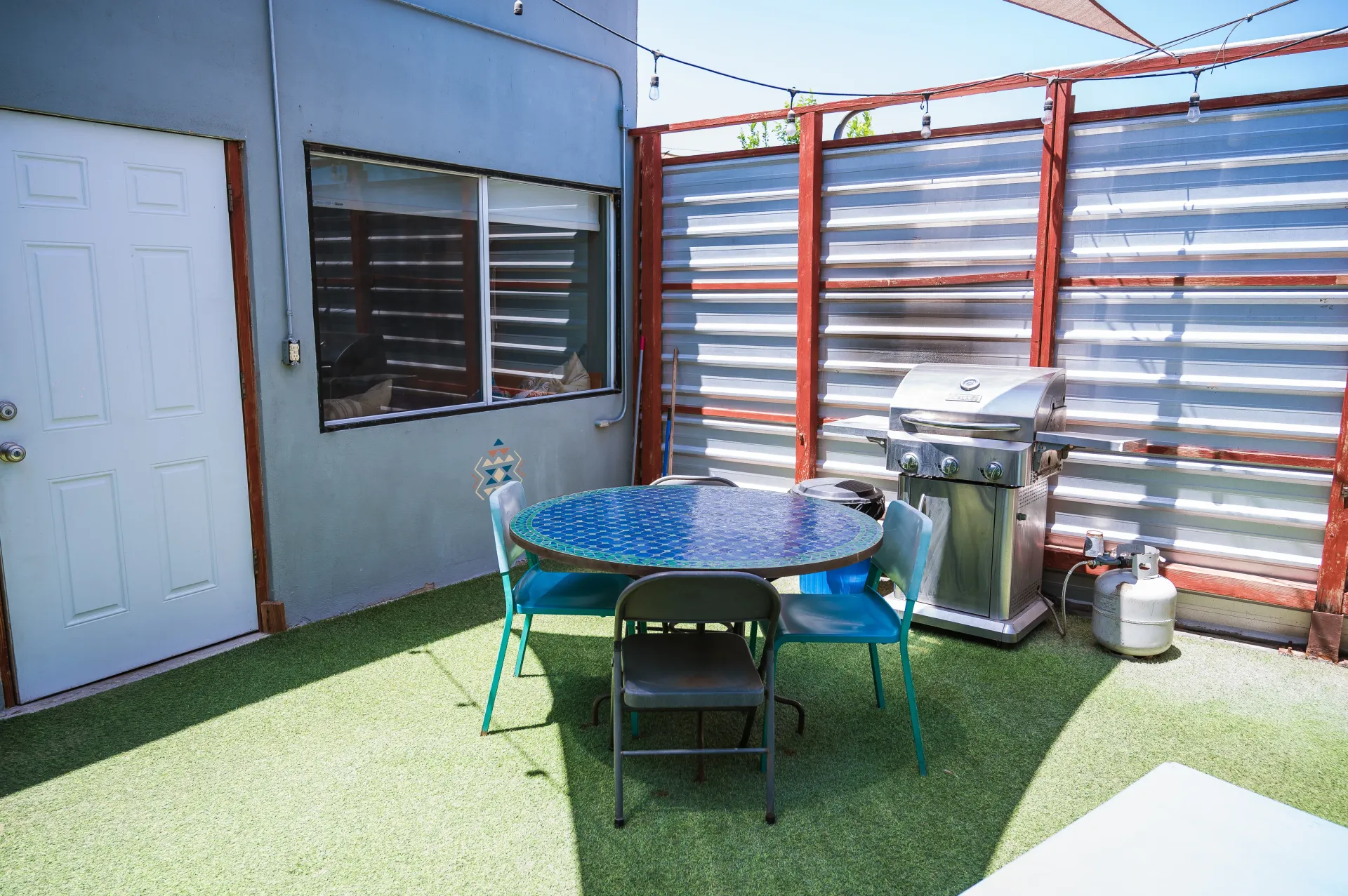 Outdoor patio with a table and grill. The walls are corrugated metal and the ground is green.
