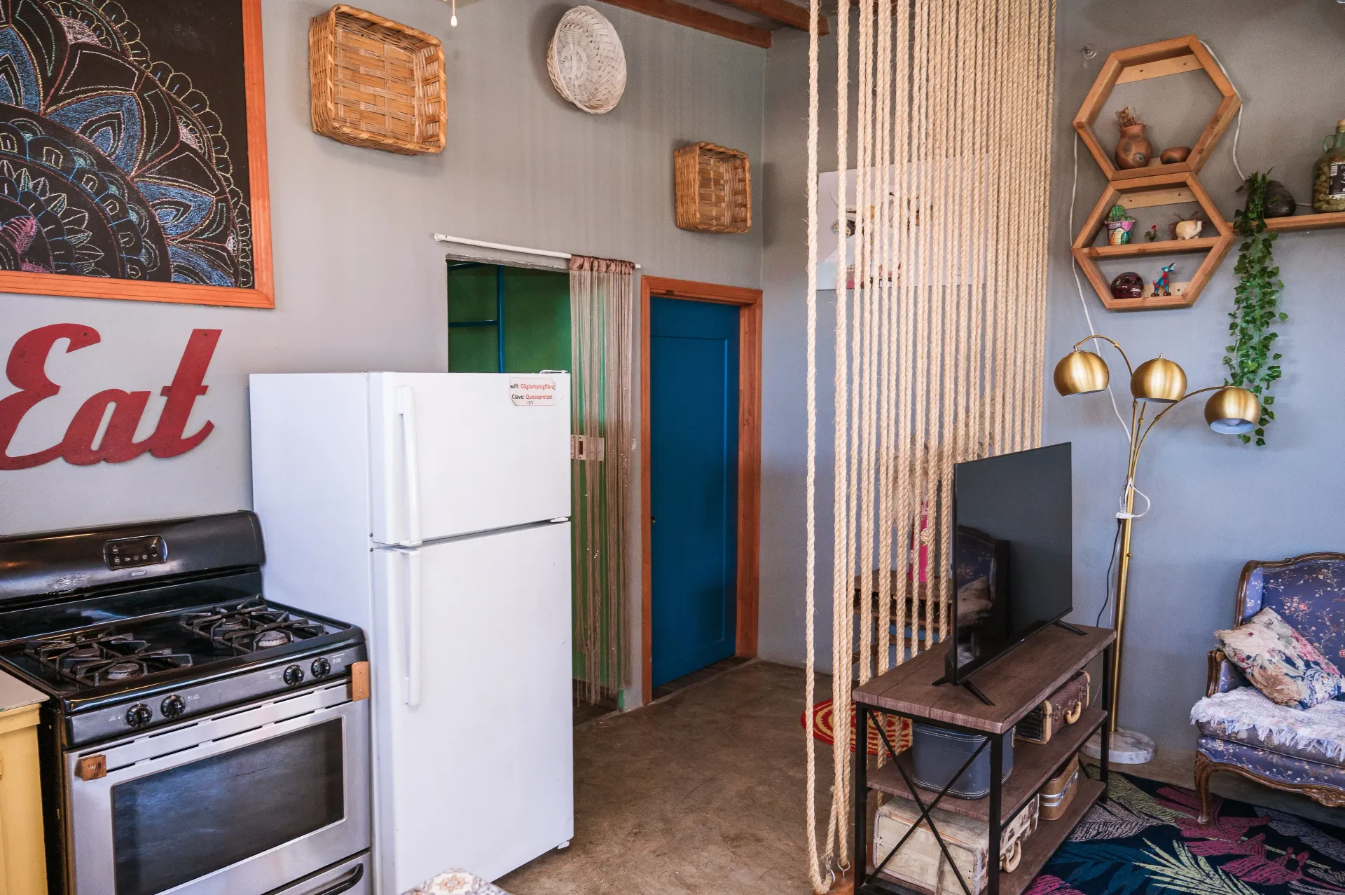 A small, eclectic living space with a kitchen, seating area, and bead curtain.