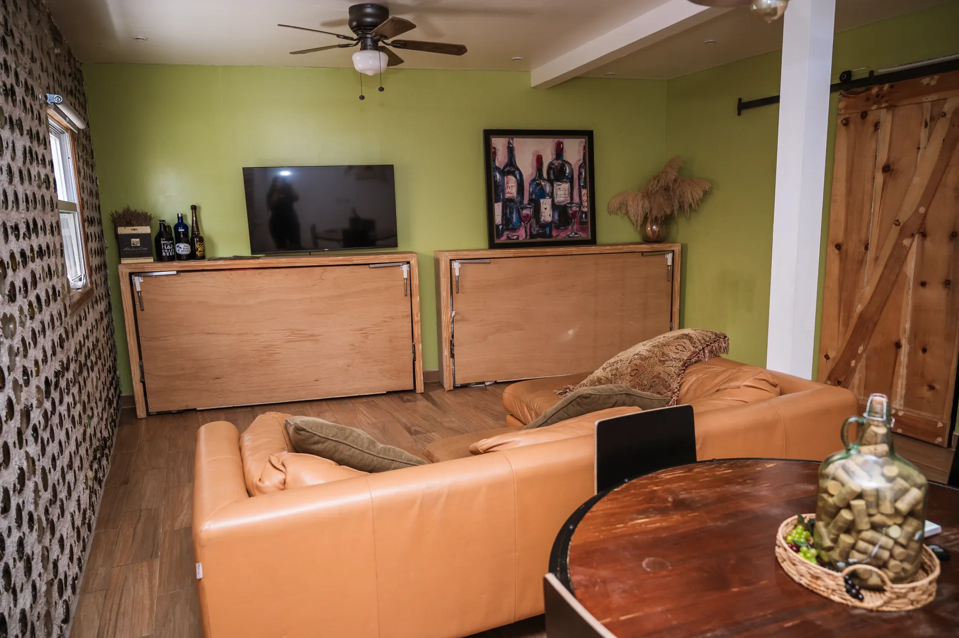 Cozy living room with tan sofa, round wooden table, TV, and art on light green wall.