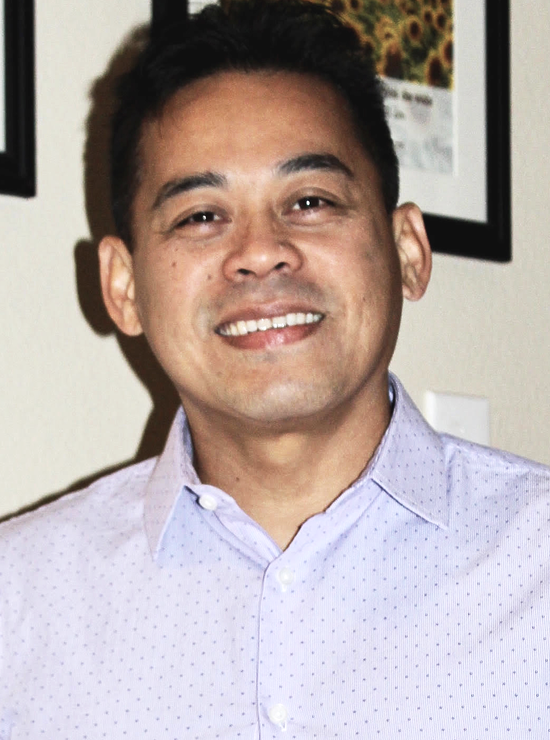 A woman is sitting at a desk with a laptop and a vase of flowers.