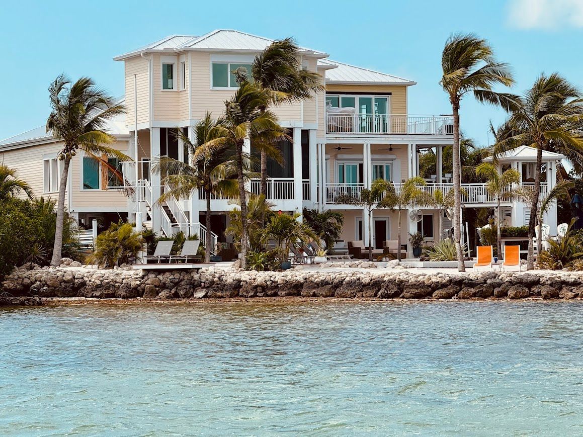 A large house is sitting on top of a tropical island next to a body of water.
