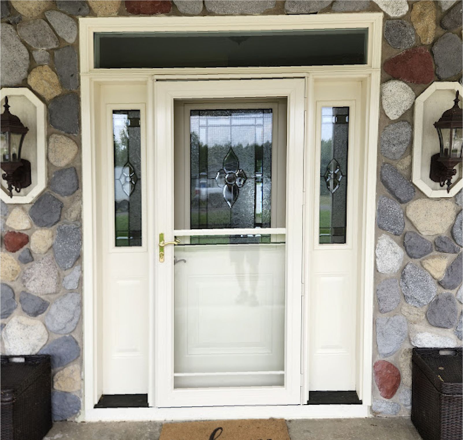 A white storm door with glass panels is centered in an entryway flanked by two sidelights, all set against a stone wall.