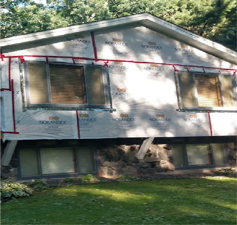 The upper level of a house exterior under construction, covered in Norandex house wrap with red seaming tape.