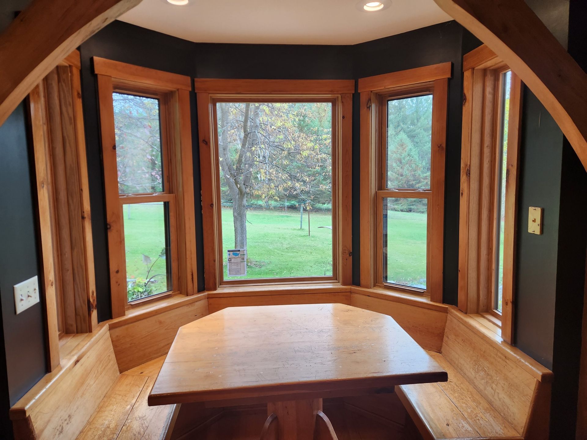 A cozy wooden dining nook with built-in bench seating arranged around a table in front of a bay window.