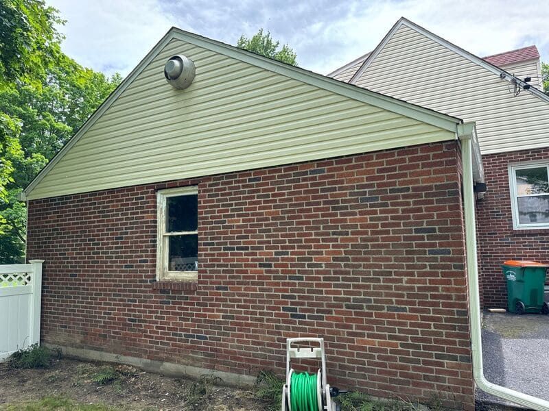 Brick house with light green siding, window, and a hose.
