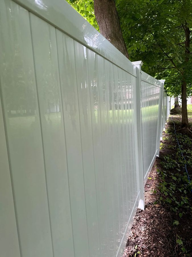 White vinyl fence in a yard, next to a tree.