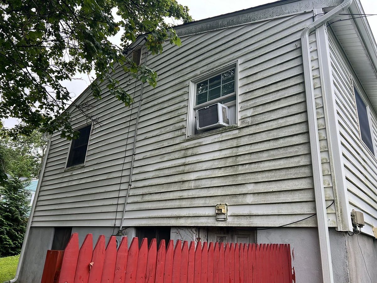 Side of a two-story house with dirty white siding and a red picket fence. Air conditioner in window.