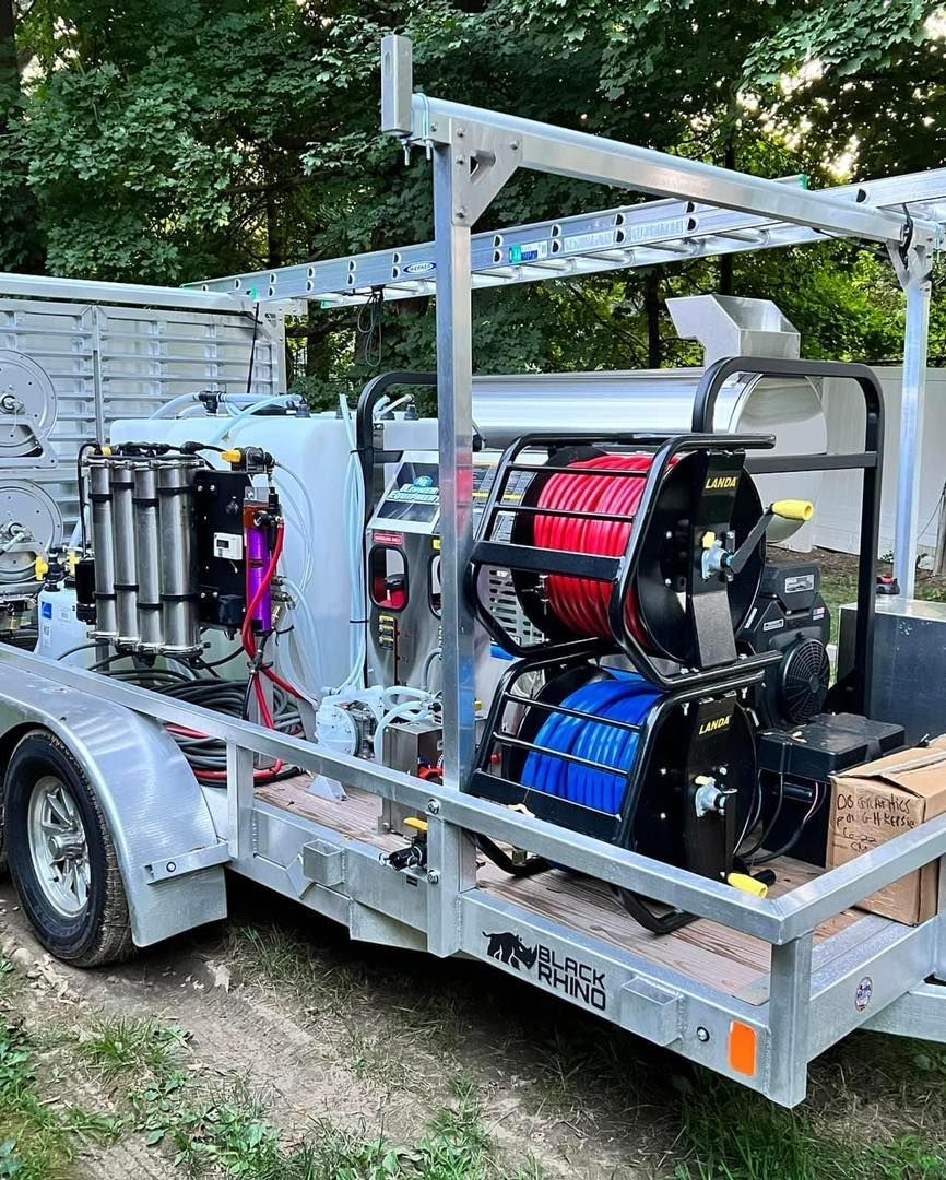 A trailer with cleaning equipment, including hoses, tanks, and a reel, set outside.