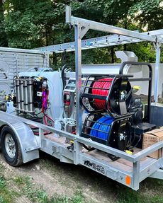 A trailer with cleaning equipment, including hoses, tanks, and a reel, set outside.