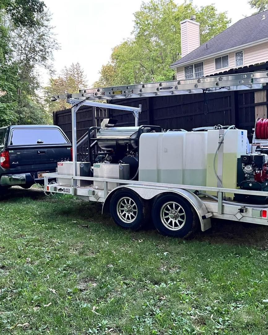 A truck towing a trailer with cleaning equipment, parked on a lawn near a house.
