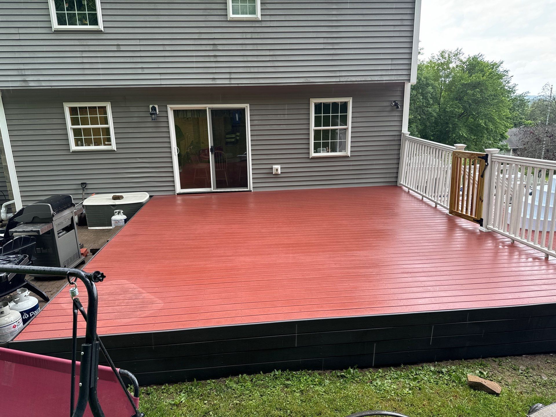 Red tiled deck on a gray house, with a glass door and white railing.