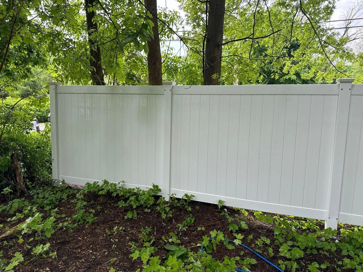 White vinyl fence in a yard, with trees and green foliage.