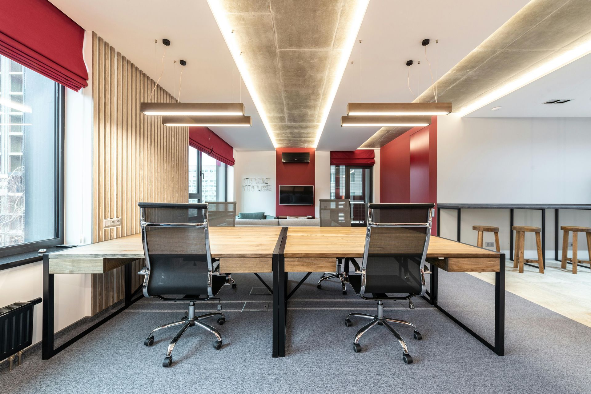 Office workspace with desks, chairs, windows, red accents, and exposed ceiling lights.