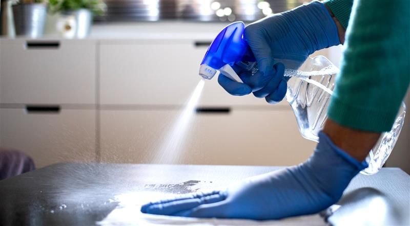 Person in blue gloves spraying cleaner on a surface, cleaning the kitchen.