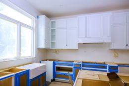 Kitchen remodel with white cabinets, unfinished lower cabinets, and a large window.