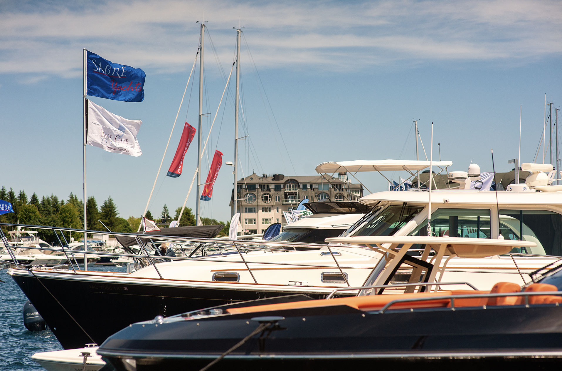A row of boats are docked in a marina with flags flying in the background
