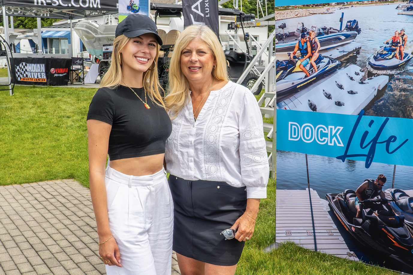 Two women are standing next to each other in front of a sign that says dock life.