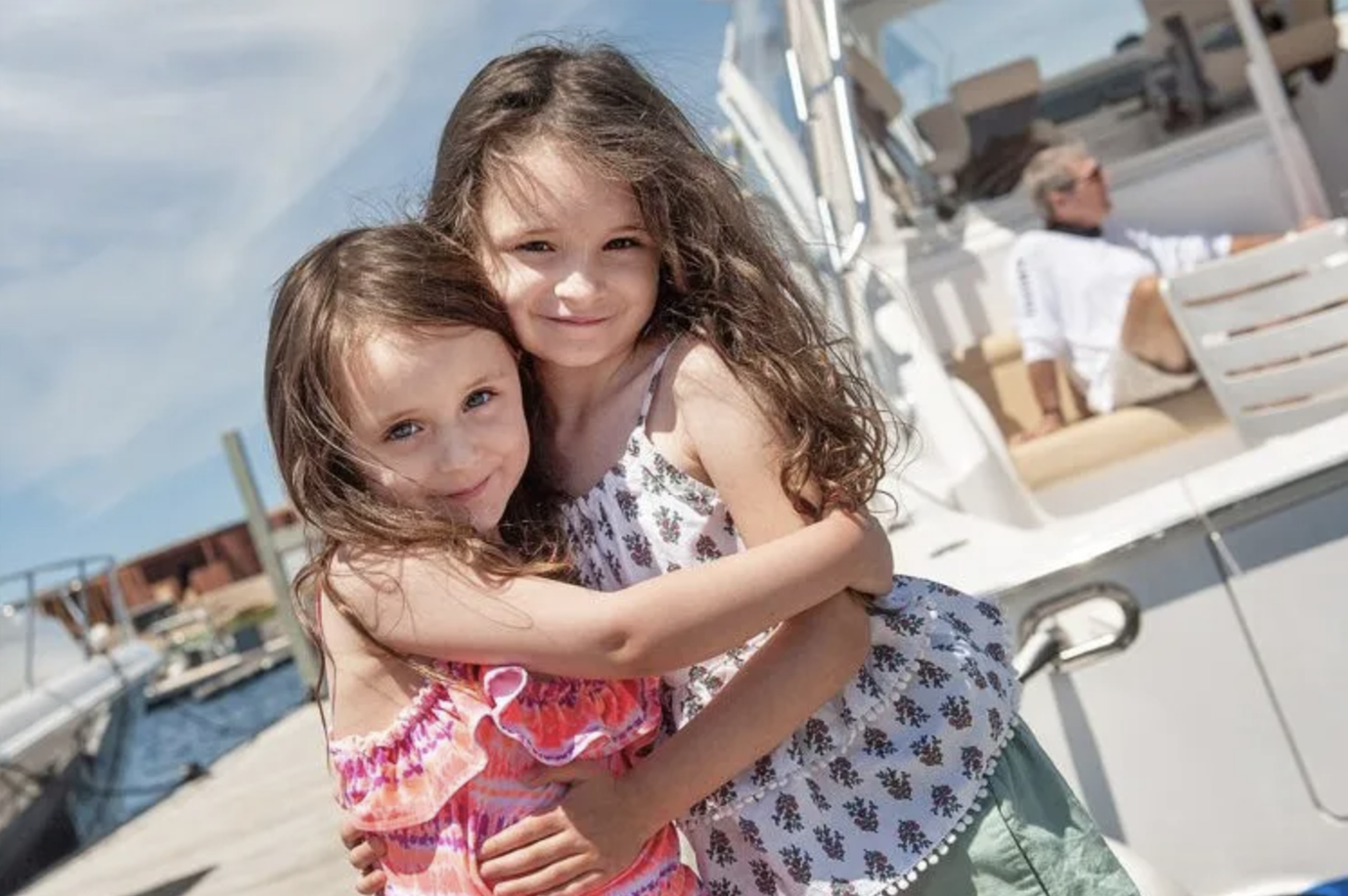 Two little girls are hugging each other in front of a boat.
