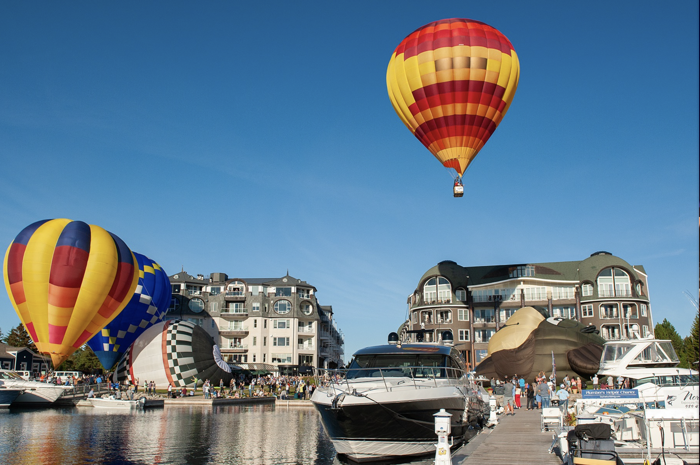 Several hot air balloons are flying over a marina