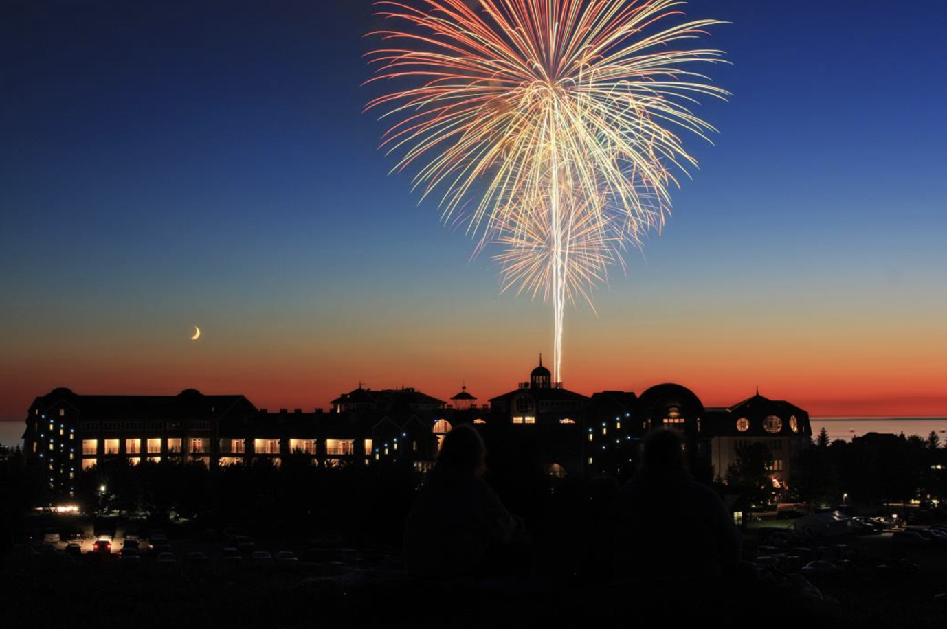 A fireworks display is taking place over a city at sunset.