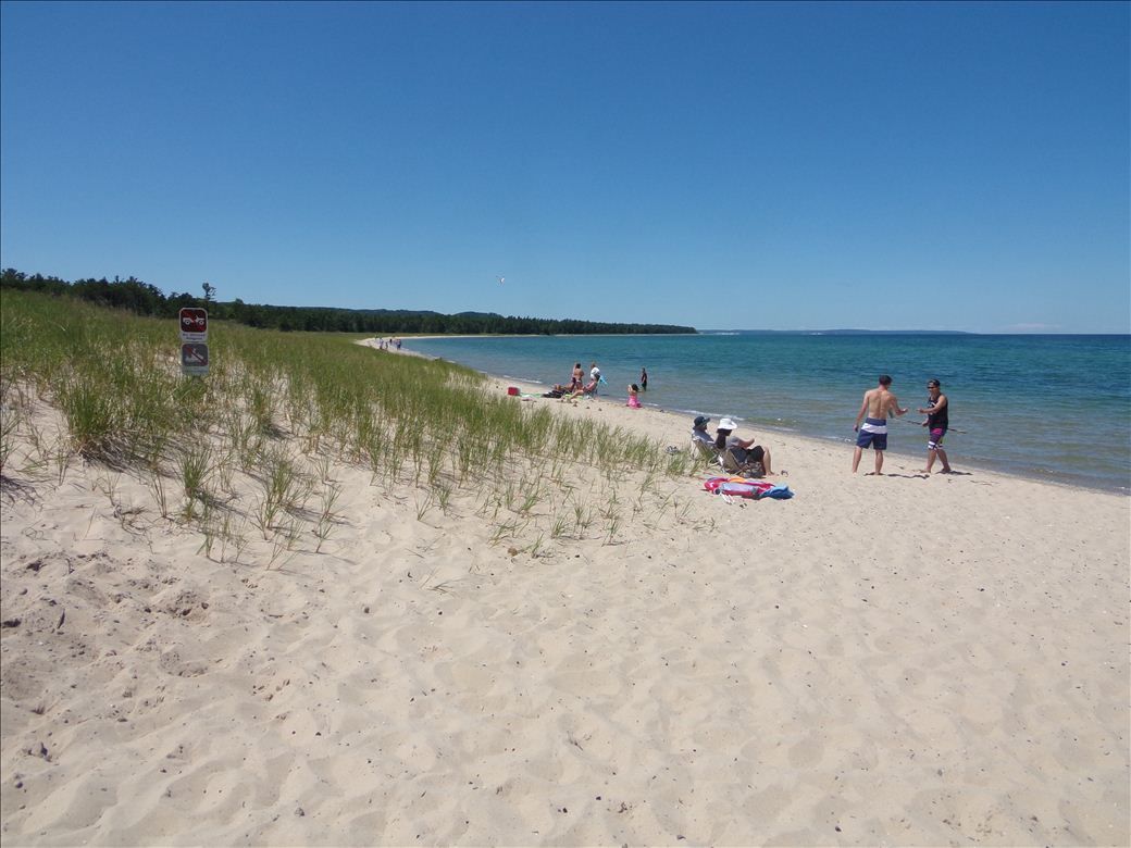 A group of people are standing on a sandy beach near the water.