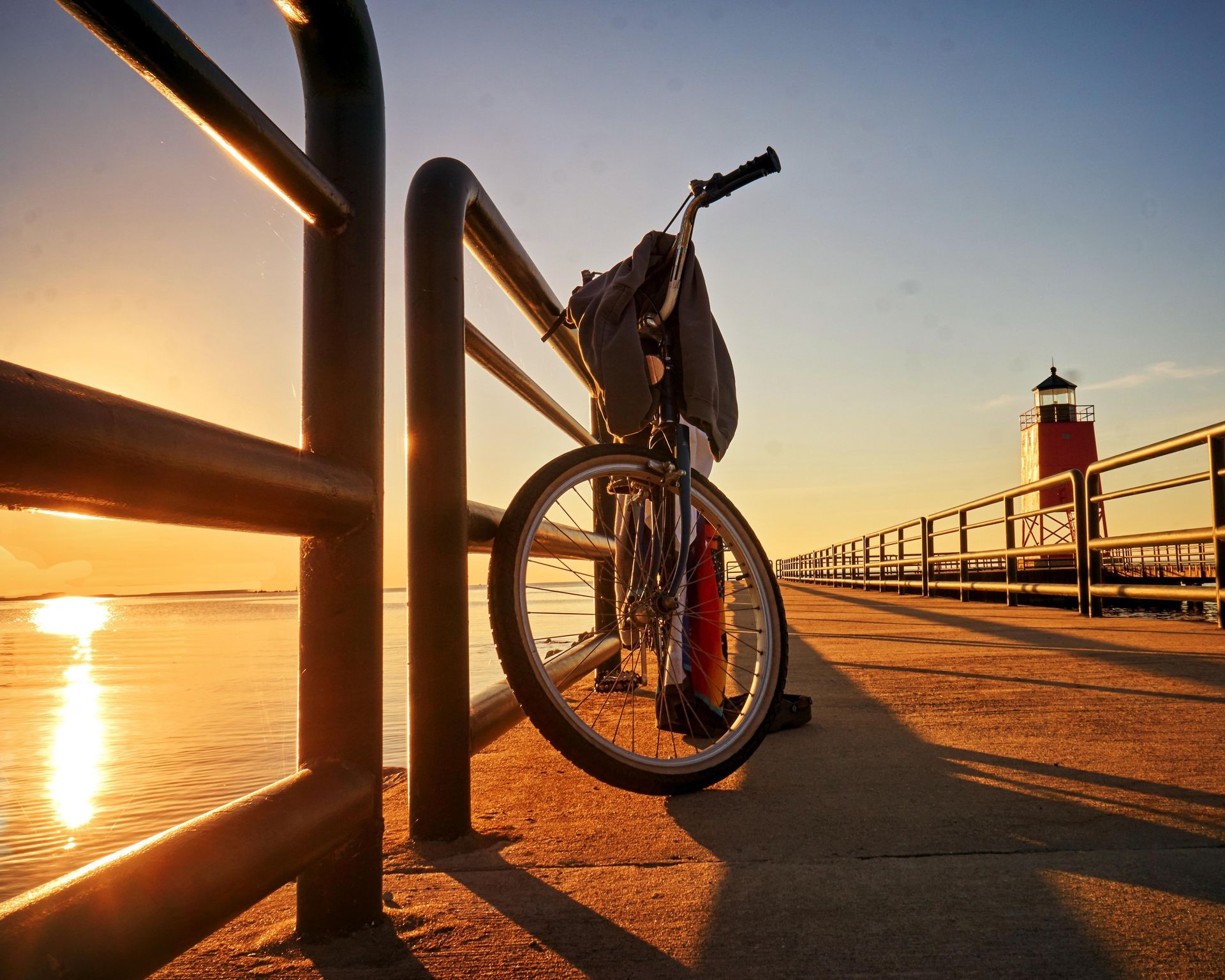 A bicycle is leaning against a railing on a pier at sunset