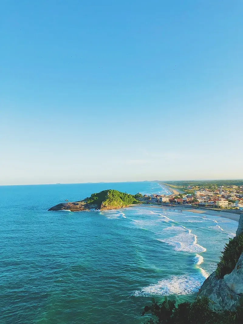 Vista aérea de um oceano turquesa encontrando uma praia de areia, com um promontório verdejante que se estende pelas águas azuis.