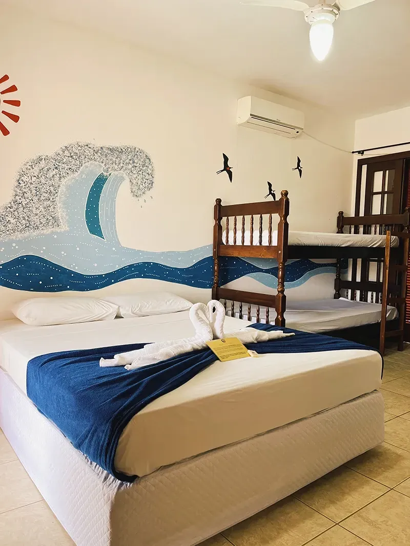 Um quarto de hotel com uma cama queen-size decorada com cisnes de toalha, um beliche de madeira e um mural de uma onda azul do oceano na parede.