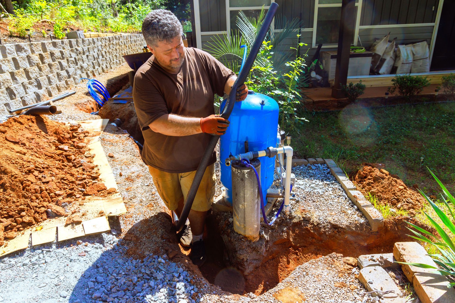 Water well drilling contractor installing blue pressure tank and piping system.