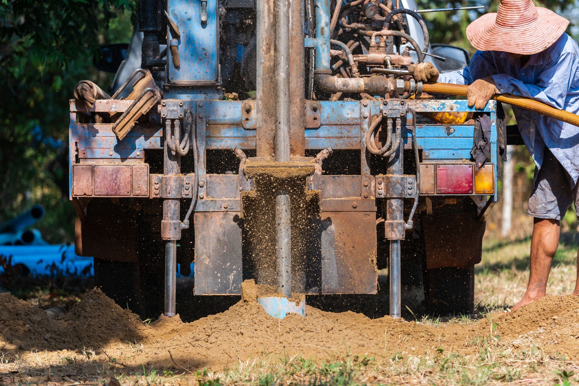 Drilling rig boring into ground as worker operates equipment outdoors.