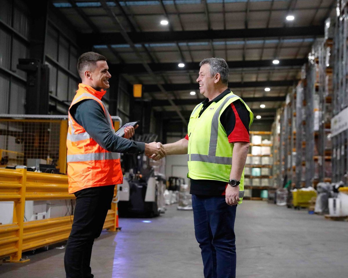 Two men are shaking hands in a warehouse. Bodycare and the client.