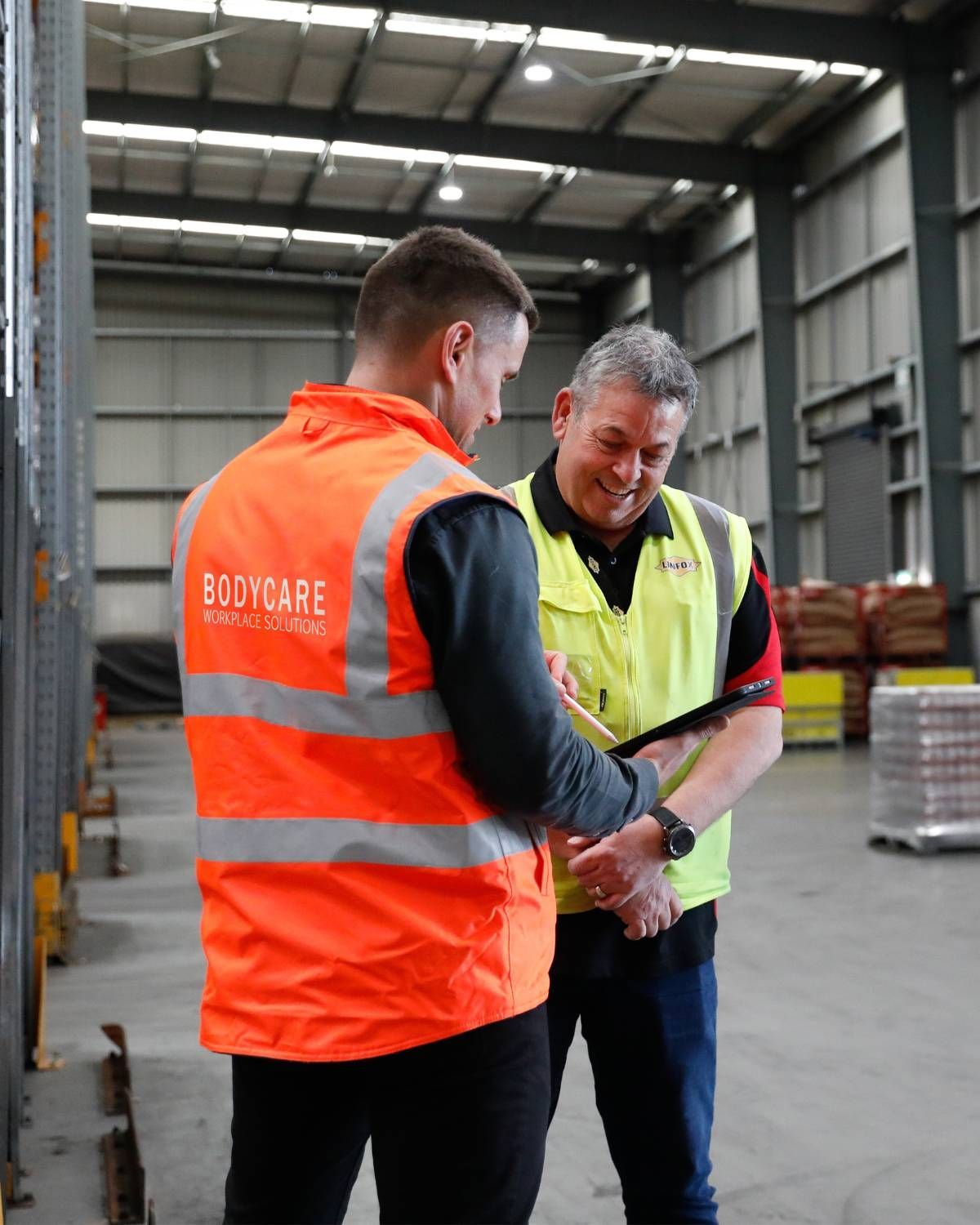 Two men in safety vests are standing in a warehouse