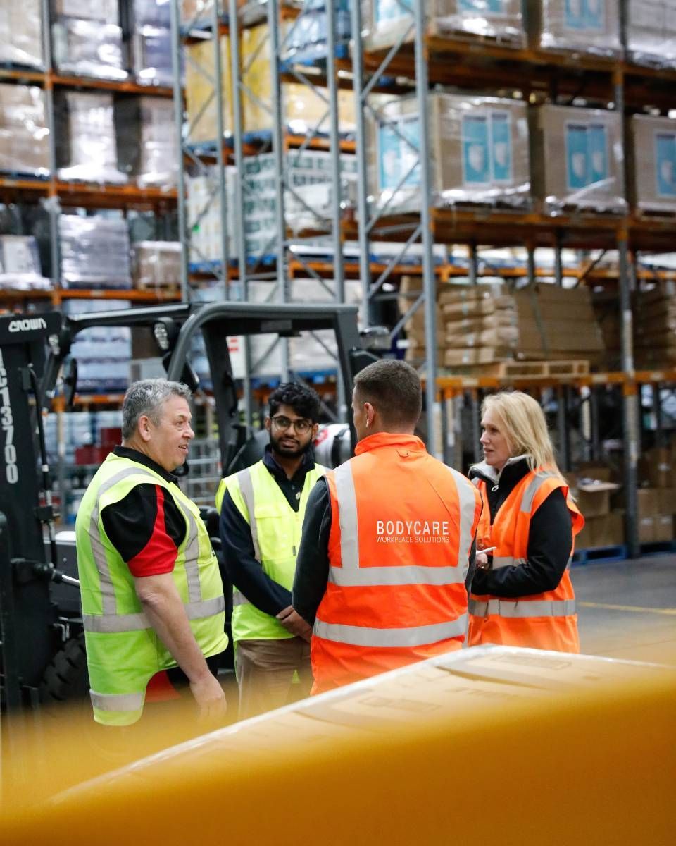 Bodycare team and clients standing in a warehouse talking to each other.