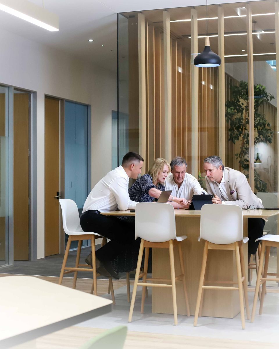 A group of people are sitting around a table looking at a tablet.