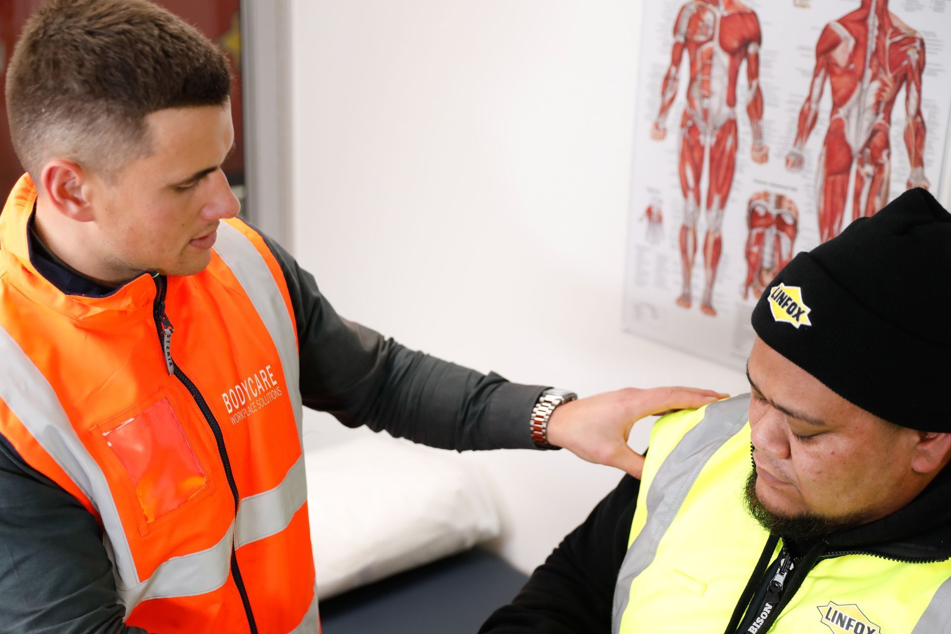 A bodycare employee in an orange vest is talking to another man in a yellow vest.