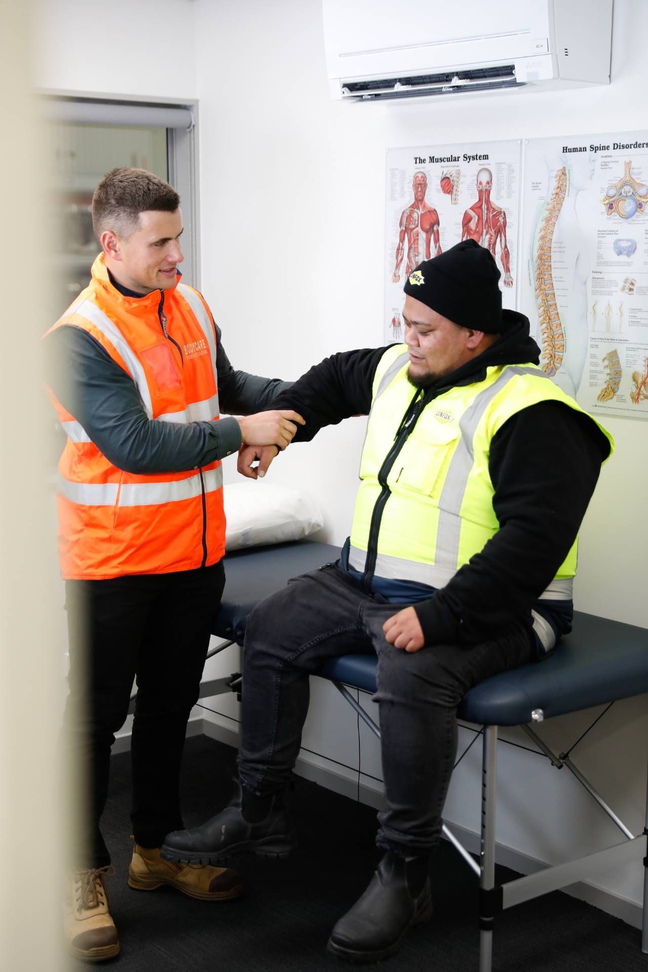 A man in an orange vest is shaking hands with a man sitting on a table.