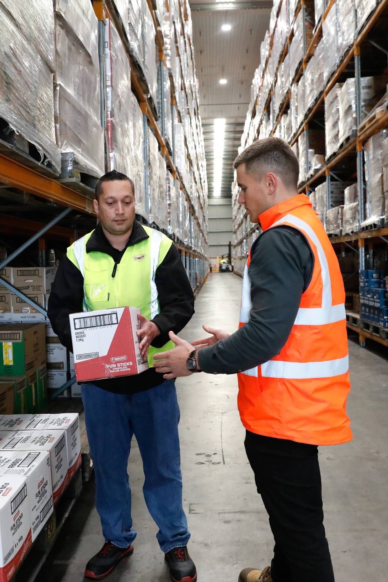 Two men are standing in a warehouse talking to each other.