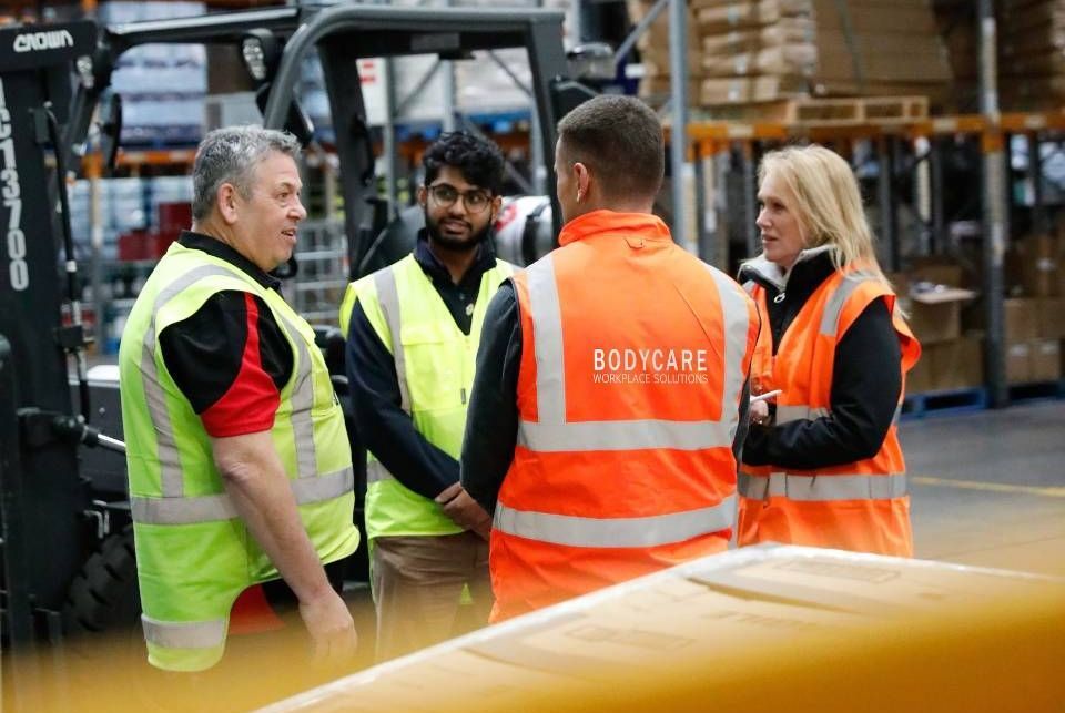 A group of workers are standing in a warehouse talking to each other. Bodycare and the clients.